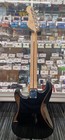 Black SQUIER Bullet Strat electric guitar with light wood back and silver hardware, displayed in a retail store window.