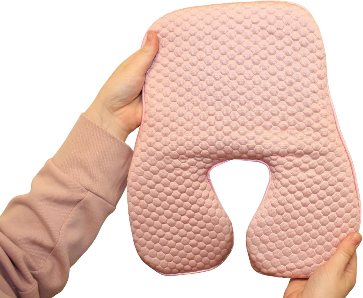 Hand holding a pink gel polymer and memory foam cushion with textured hexagonal pattern, resting on white background.