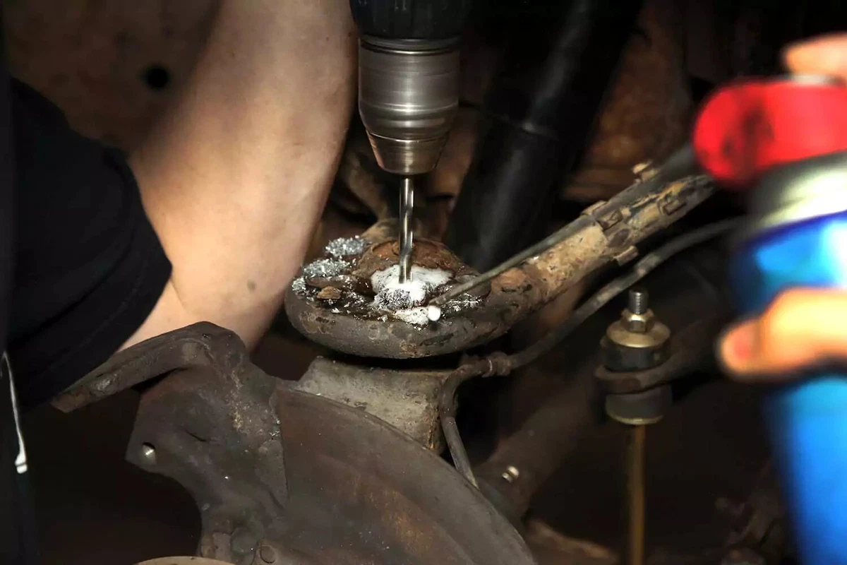 A mechanic drills out a rivet stalk using a power drill and a can of spray lubricant.