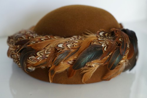Brown hat with 100% wool EXCELLO, featuring colorful pheasant and quail feathers with patterned brown, black, and white plumage.