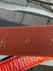 Brown leather belt with gold-tone embossing of “42 Made in U.S.A.”, featuring coiled orange leather strap.