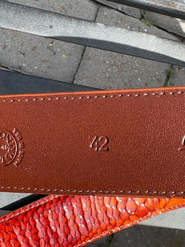 Brown leather belt with gold-tone embossing of “42 Made in U.S.A.”, featuring coiled orange leather strap.