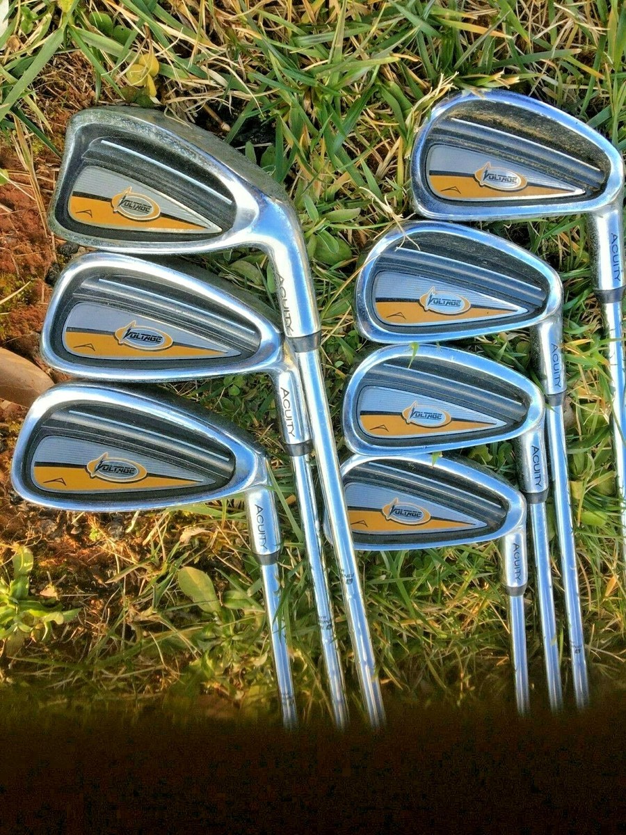 A Full Set Of Acuity Voltage Golf Clubs, Including Irons, Woods, And A Putter, Laid Out On A Patch Of Grass And Dirt, Ready For A Beginner To Use.