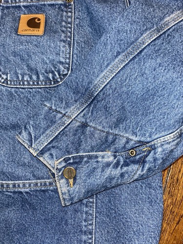 Blue denim Carhartt C59 DST chore coat with front pocket, button cuffs, and visible Carhartt logo patch on chest.