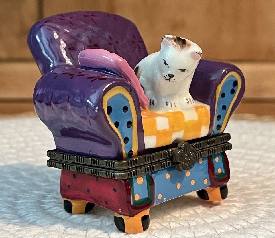 A hand-painted miniature trinket box featuring a kitten lounging on a purple tufted armchair — tiny, detailed, and deeply charming.