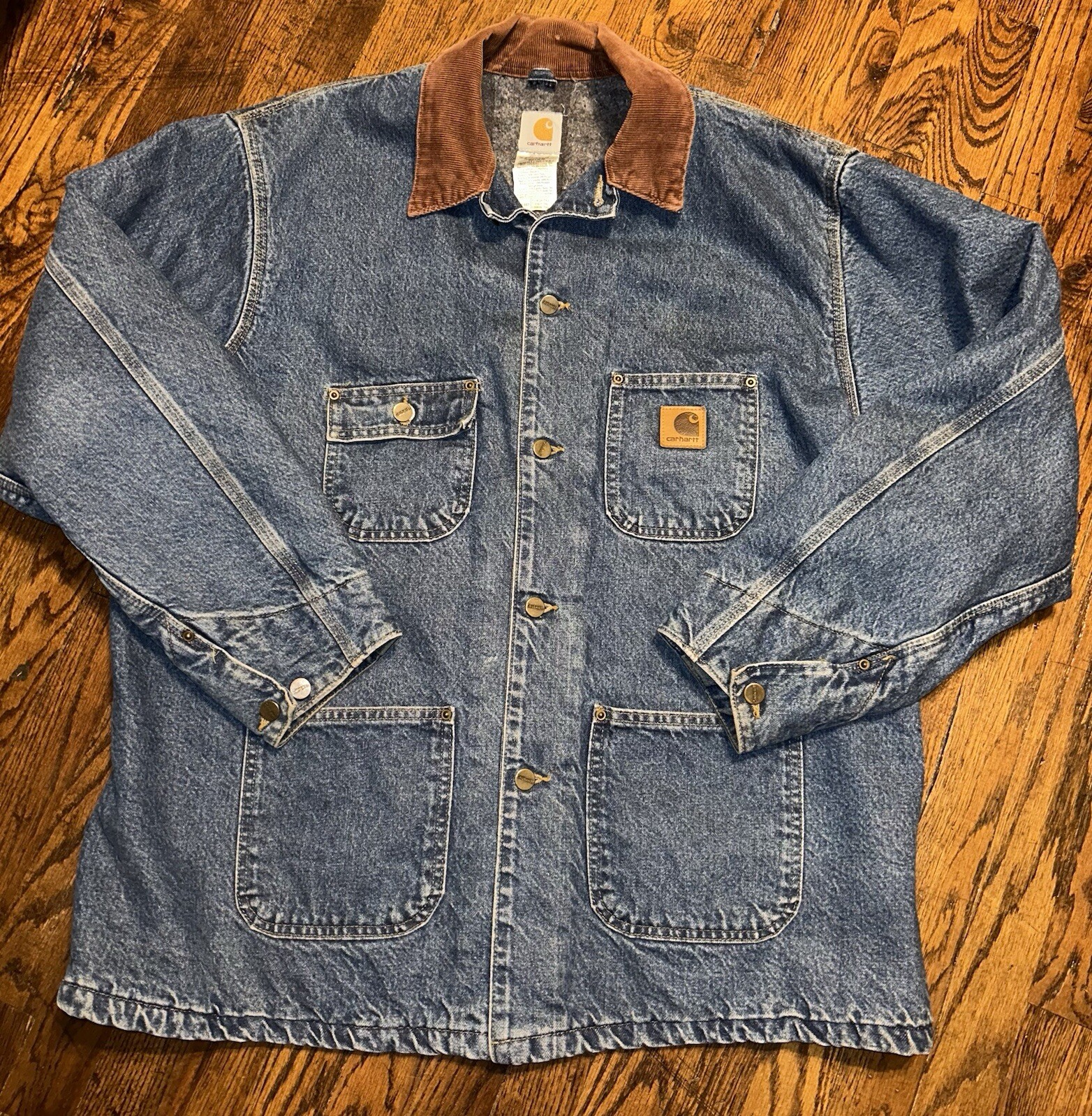 Blue denim Carhartt C59DST chore coat with brown collar, front button closure, and small yellow Carhartt logo patch.