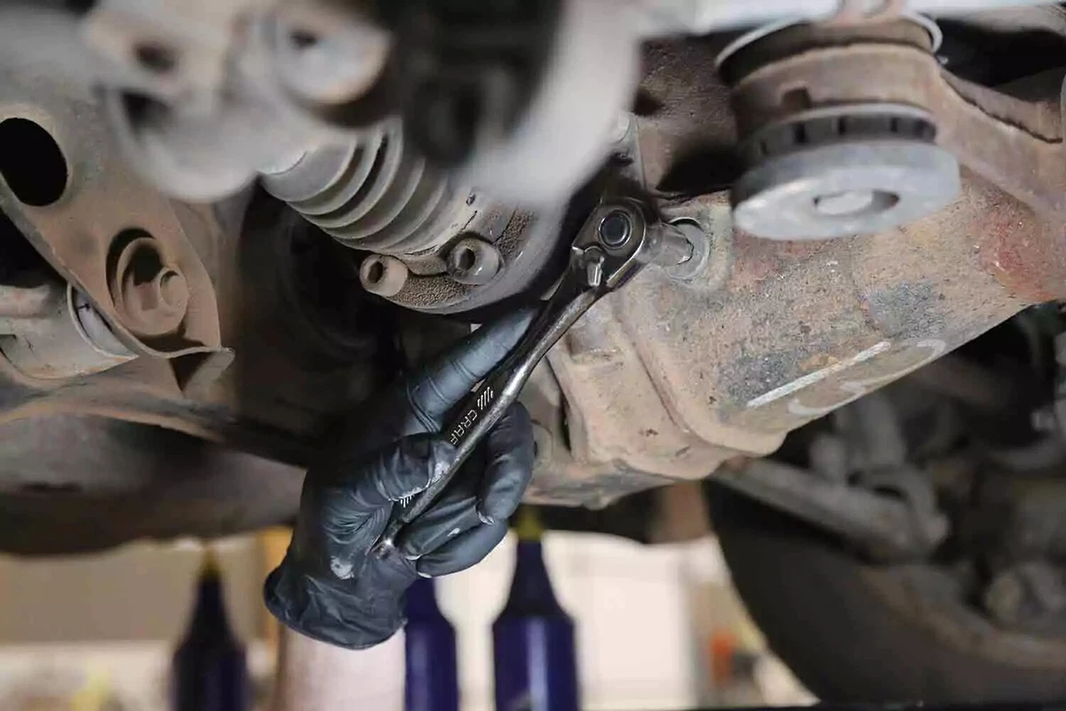 A mechanic wearing a black glove uses a socket to remove the fill plug of a vehicle's rear differential.