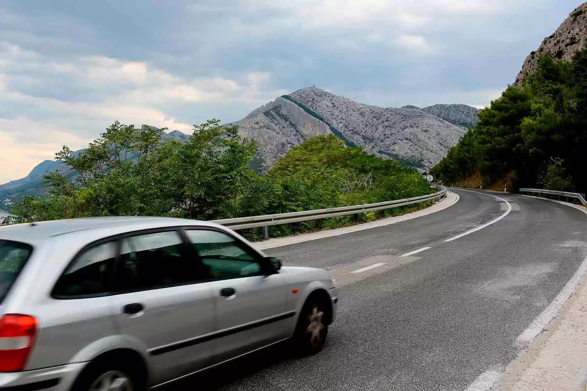 A silver car driving at speed on a twisty mountain road.