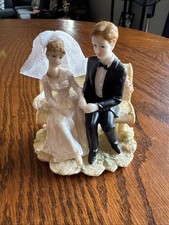 vintage 1980s cake topper features a bride and groom sitting together on a bench