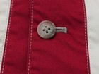 Faconnable medium red quilted vest with white stitching and a round button closure on a striped fabric background.