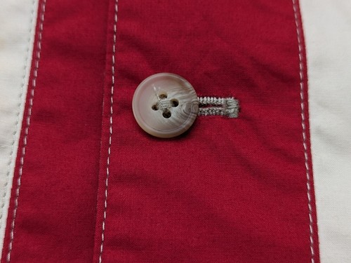 Faconnable medium red quilted vest with white stitching and a round button closure on a striped fabric background.