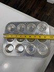 Silver 12-cup mini muffin pan with black circular muffin cups, shown on white surface beside yellow measuring tape.
