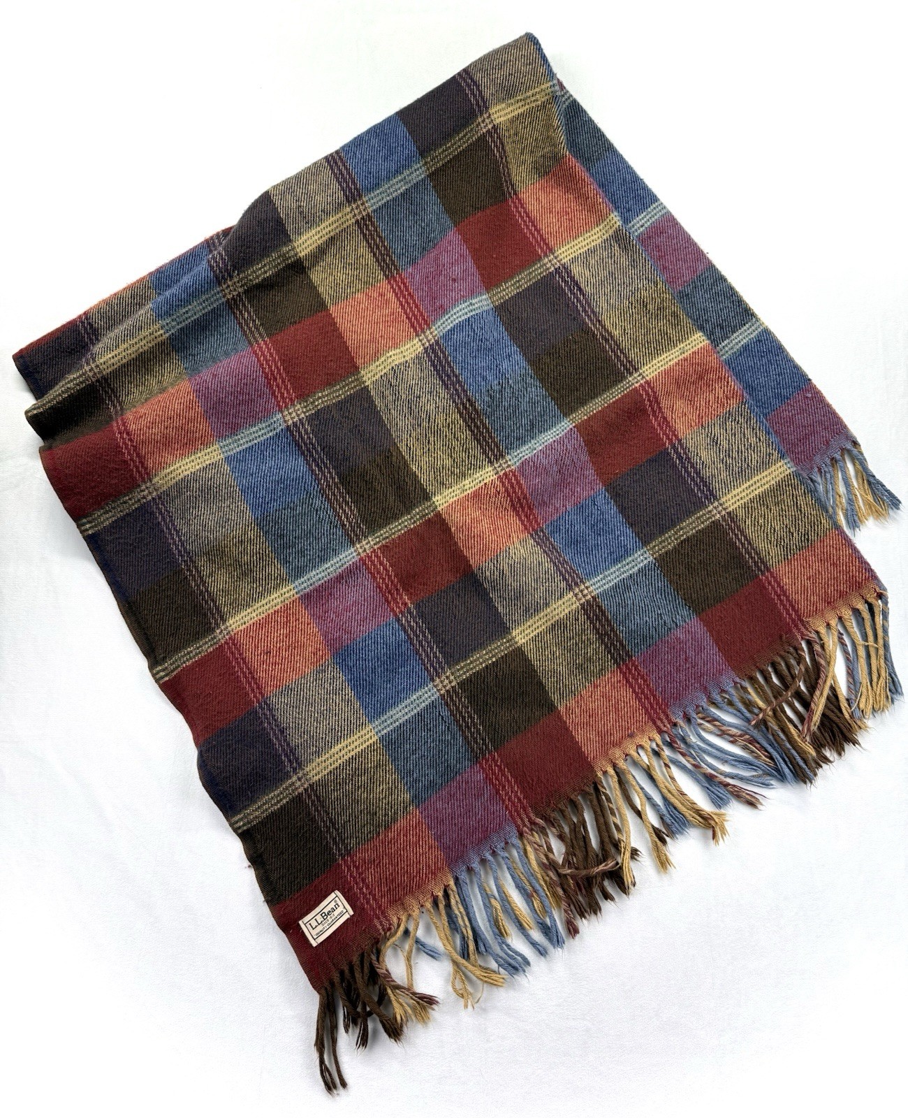 Red and blue plaid wool throw blanket folded to show the tartan pattern and fringe edge.