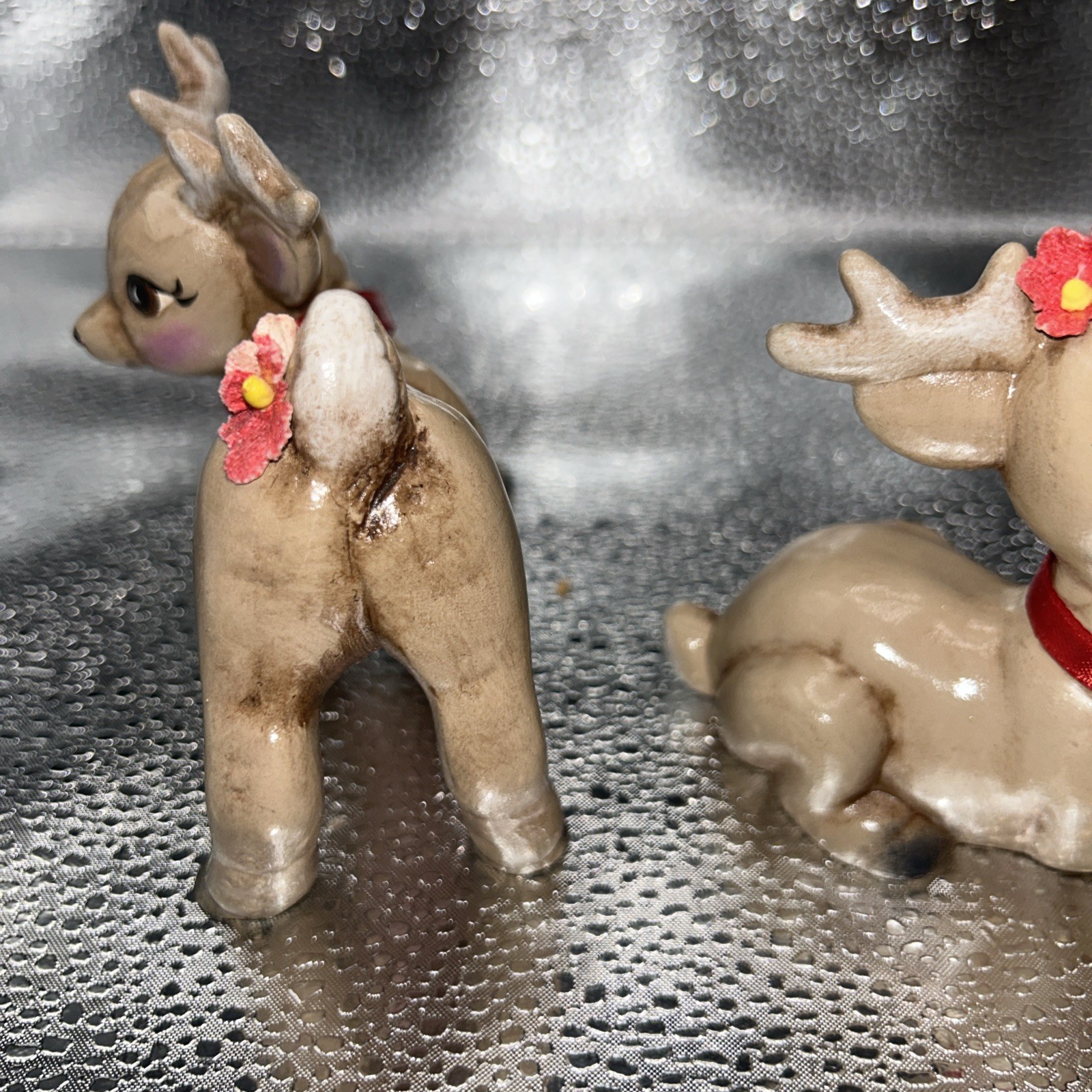 Pair of vintage Christmas reindeer babies, one lying on silver with red flower, one standing with silver antlers and red collar.