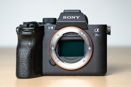 Black Sony Alpha a7S III camera with orange ring, silver body, two black batteries, and green-black sensor window.