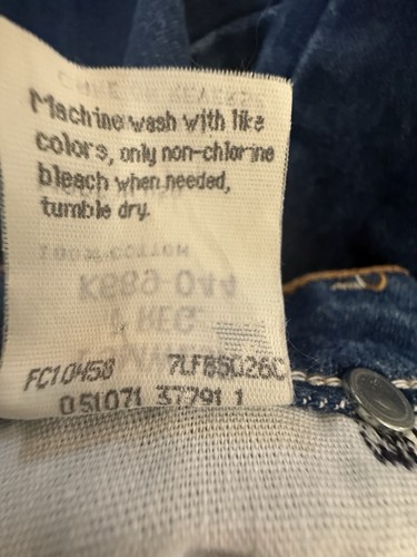 White fabric tag on waistband of blue denim cowboy jeans, size 7, with yellow printed text and black button closure.