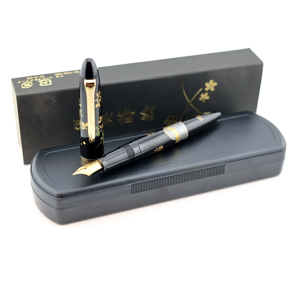 Black Sailor Maki-e fountain pen with gold floral and samurai design, displayed on box and worn on hand.