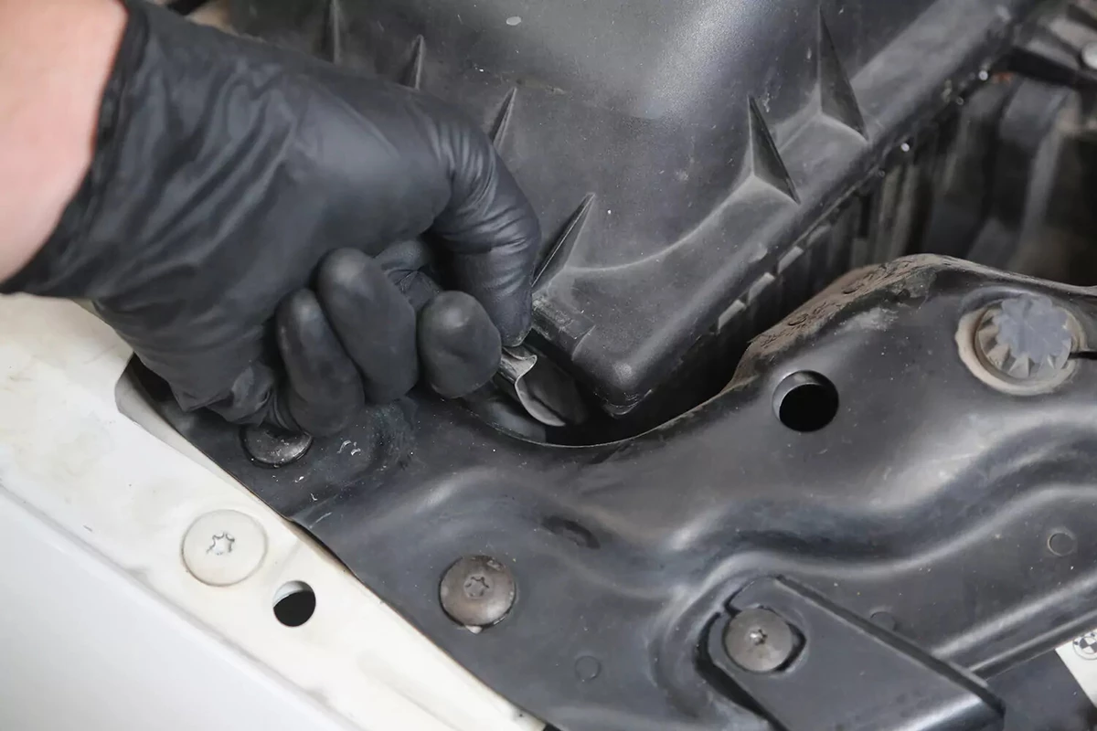 A mechanic wearing a black glove pops open a clip on the engine air filter box.