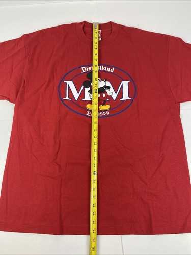 Red vintage Disneyland T-shirt with blue Mickey Mouse logo and “Disneyland Est. 1955” text, shown flat with yellow measuring tape.