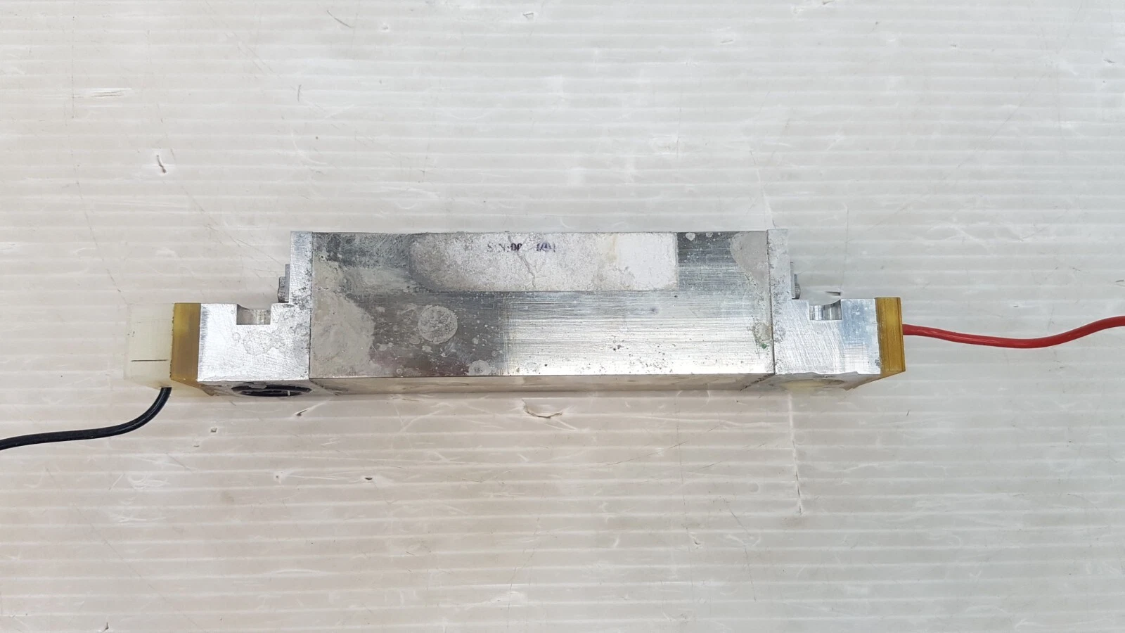 Side view of the Lumenis long brick: metal block between two end blocks, black and red leads