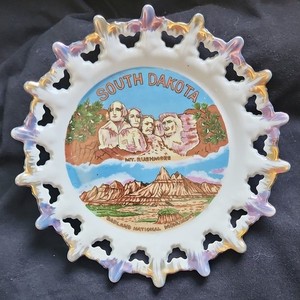 A vintage South Dakota souvenir plate featuring Mount Rushmore and Badlands.