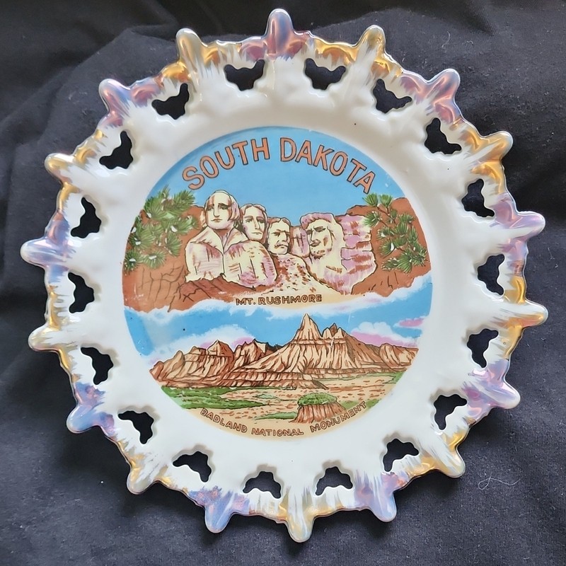A vintage South Dakota souvenir plate featuring Mount Rushmore and Badlands.