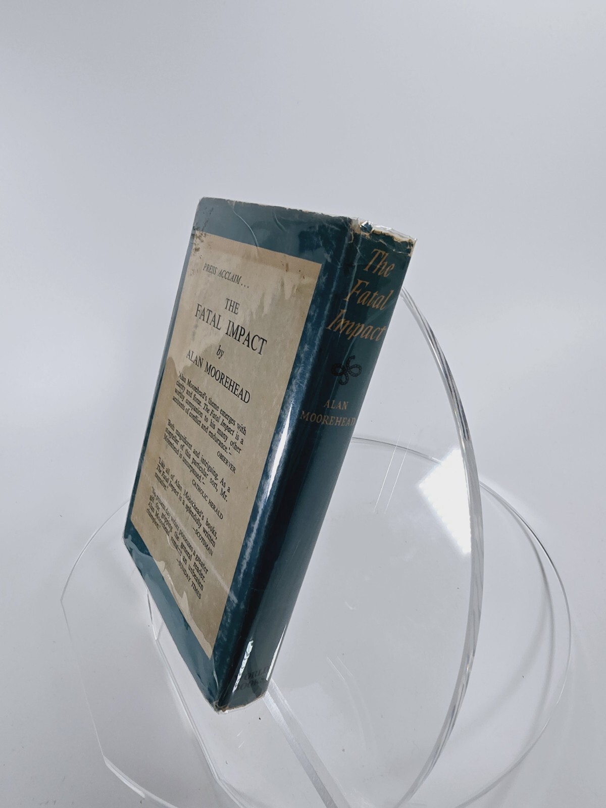 Blue hardcover book with gold text reading “The Fatal Impact” by Alan Moorehead, leaning against a clear display stand.