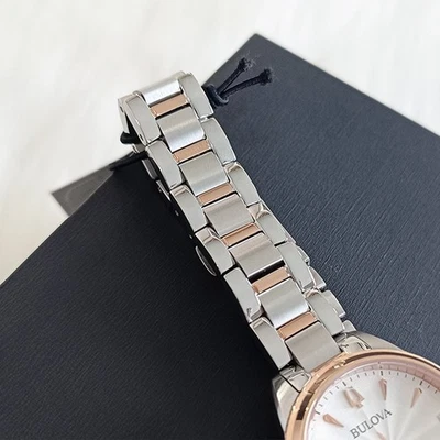 Pulsera de cadena de plata y oro rosa con esfera blanca, reloj Bulova 98P200, caja de 28 mm, sobre fondo de tela negra.