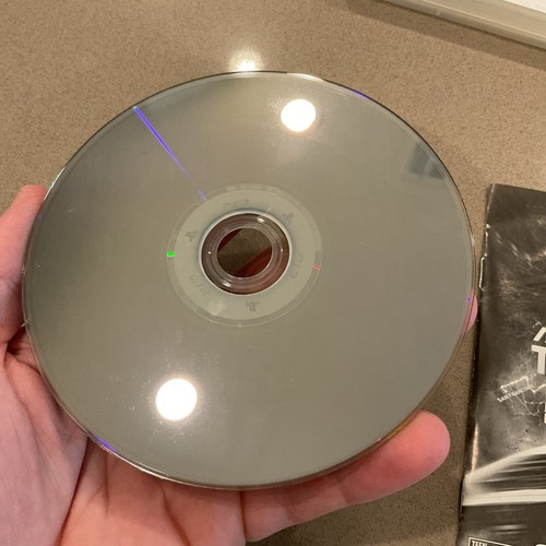 Hand holding a silver PlayStation 3 game disc with rainbow-colored spirograph pattern and black text label.