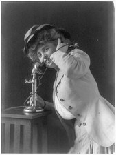 Woman holding up telephone receiver,coat,hat,clothing,communication,c1907