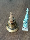 Gold-toned Liberty Bell trinket boxes with raised white Statue of Liberty figures on a wooden surface.