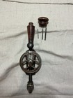 Vintage hand crank drill with worn wooden handle, two metal drill bits, and a round wood storage handle on fabric background.