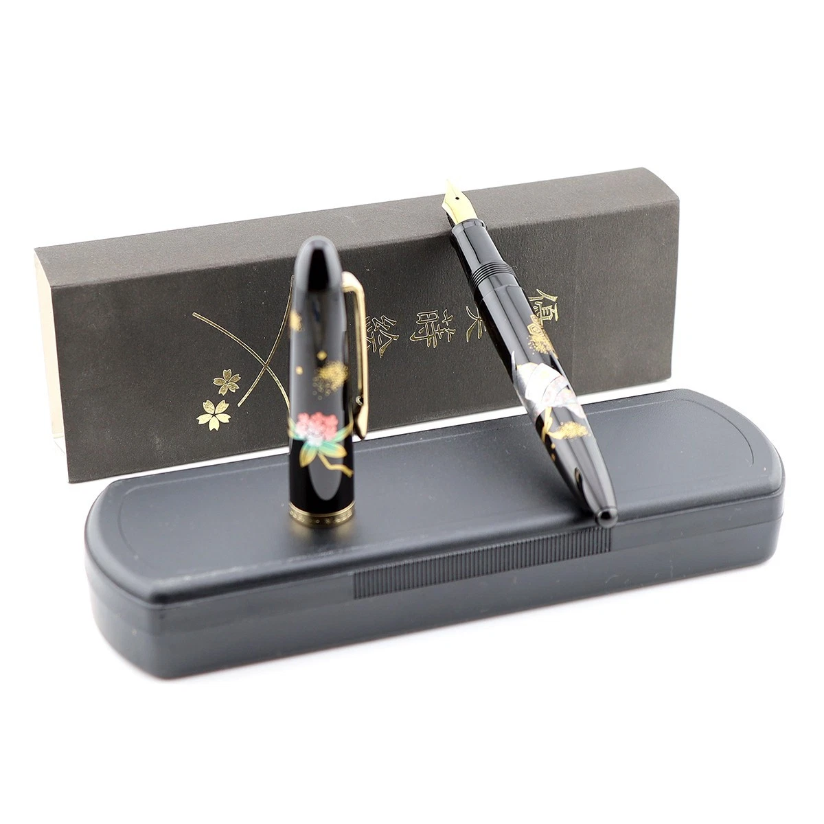 Black Sailor Maki-e fountain pen with gold accents, surrounded by pink cherry blossom design, on display in black box.