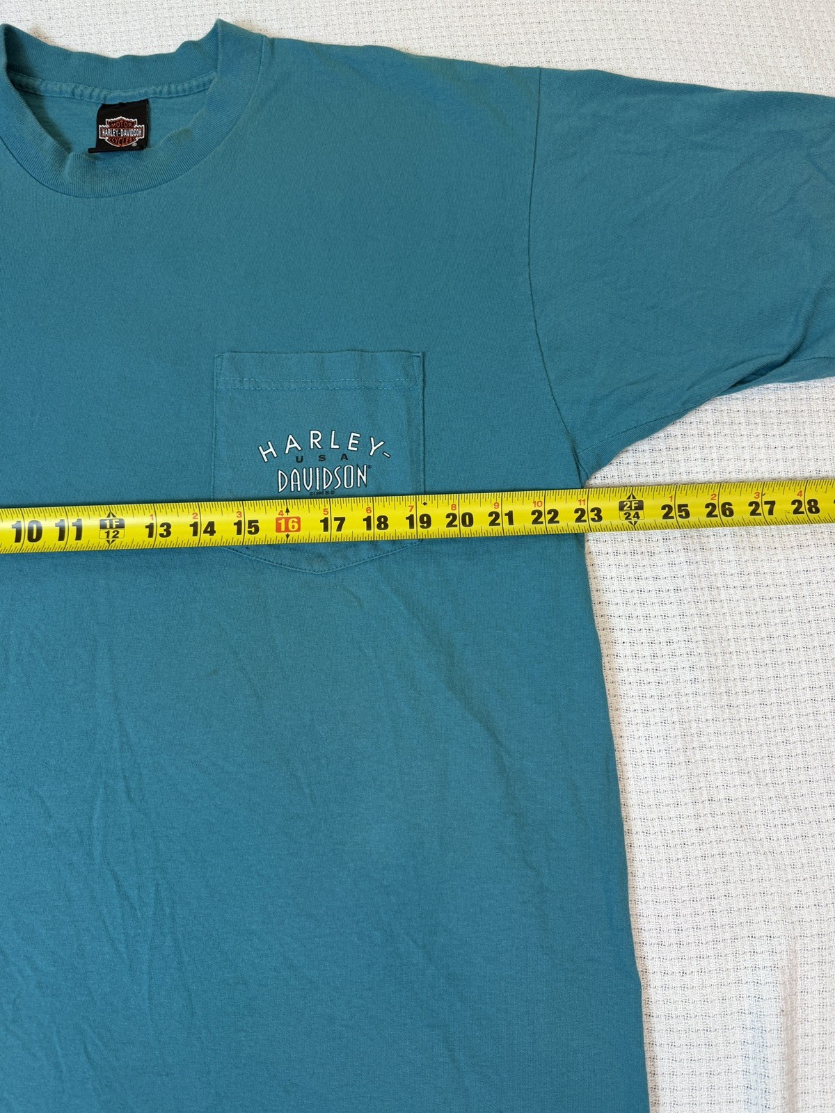 Teal Harley-Davidson men’s XL T-shirt with front pocket, yellow measuring tape, and white “Harley-Davidson Made in USA” text.
