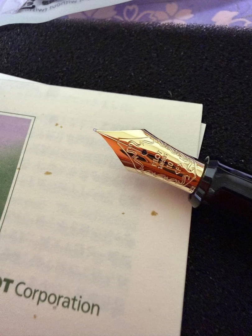 Gold-toned UNUSED Pilot fountain pen with black nib on purple “Phoenix Urushi Makie” card, white body with gold lettering.