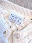Cream knit women's long sleeve sweater with scalloped lace pattern, button closure, and white tag reading “MADE IN U.S.A.”