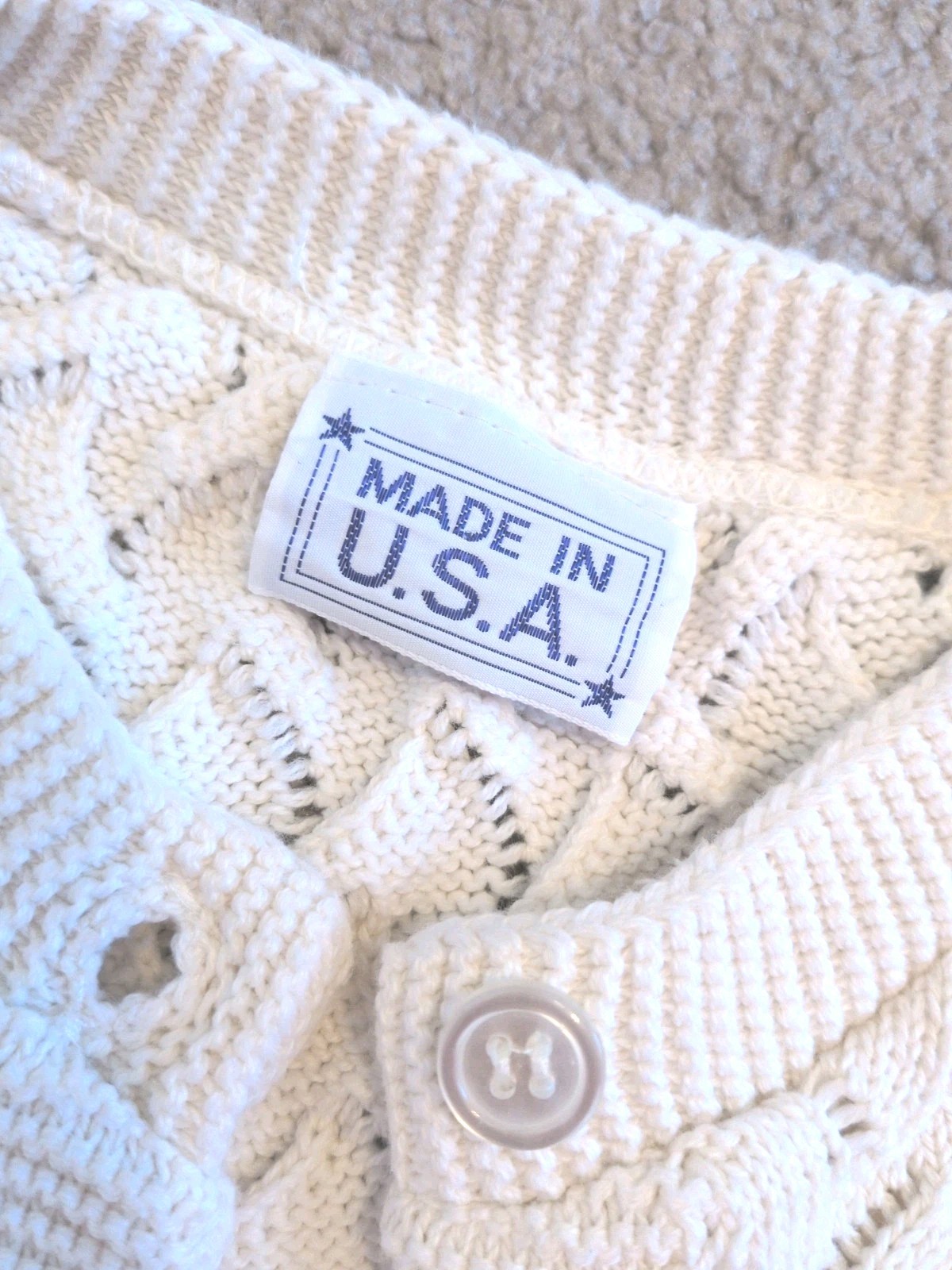 Cream knit women's long sleeve sweater with scalloped lace pattern, button closure, and white tag reading “MADE IN U.S.A.”