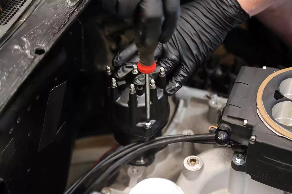 With the distributor in position, a mechanic fastens the distributor cap using a screwdriver.
