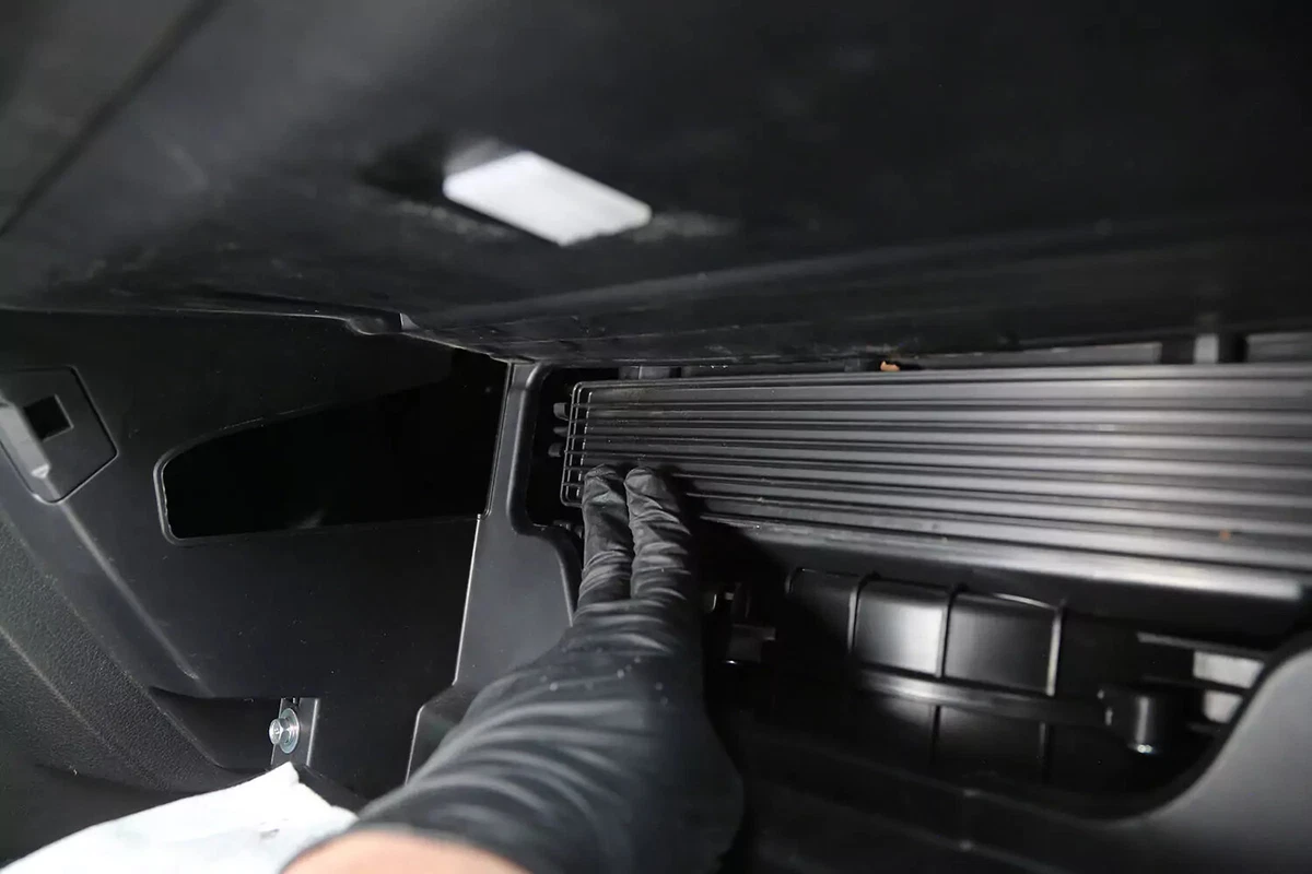 A mechanic wearing a black glove pushes the cabin air filter compartment door back into place.