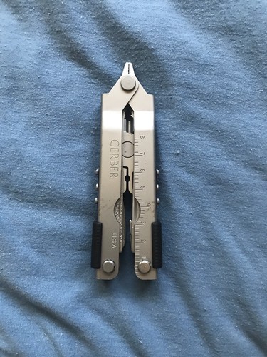 Gerber MP600 USA Made Multitool 0870314S3 with silver blade and black accents on a blue fabric background.