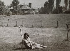 Junge Frau sitzt lasziv auf einer Wiese vor einem Haus Foto