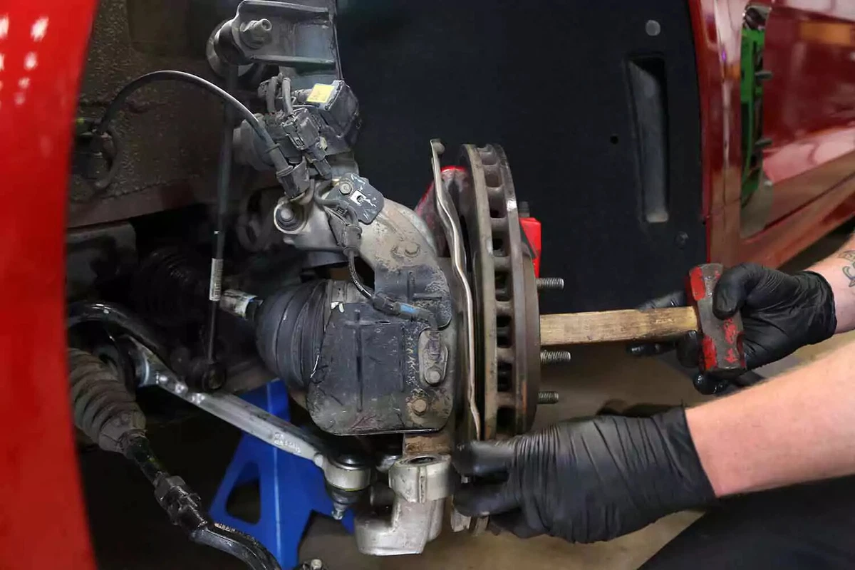 A mechanic uses the hammer handle to push the axle shaft out of the knuckle.