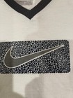 White short-sleeve T-shirt with black and gray Nike swoosh logo, black collar, and “Made in U.S.A.” label visible.
