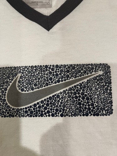 White short-sleeve T-shirt with black and gray Nike swoosh logo, black collar, and “Made in U.S.A.” label visible.