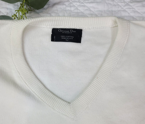 White V-neck Christian Dior men's sweater with blue text reading “100% Cotton Made in U.S.A.” on collar.