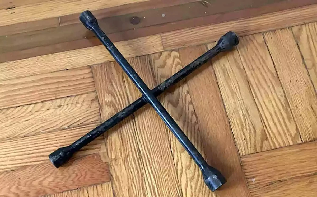 A vintage four-way tire iron displayed on a wooden floor.