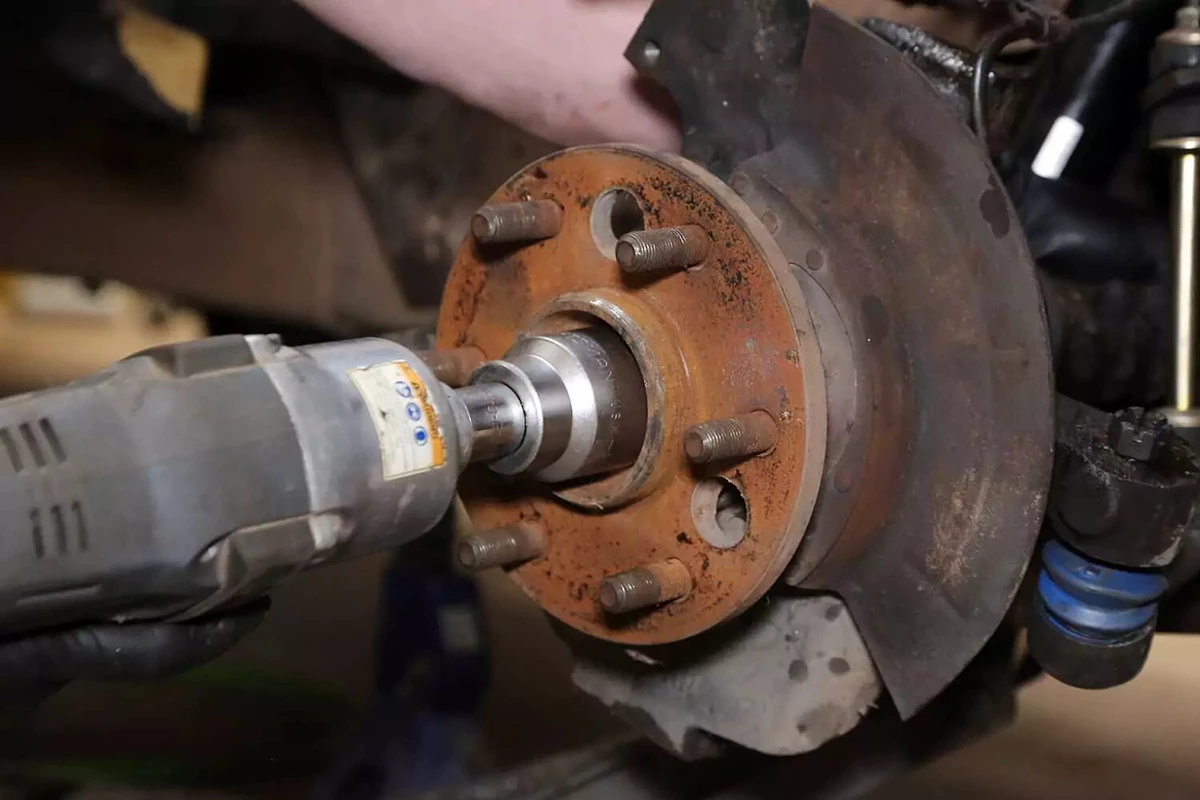 A mechanic removes an axle nut with an impact gun.