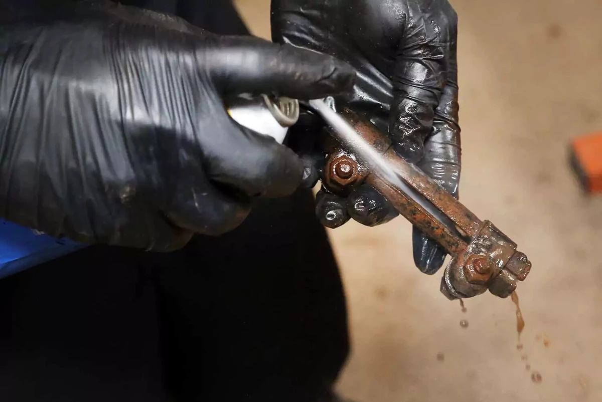 A mechanic uses brake cleaner to remove dirt from the tie rod sleeve.