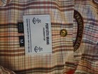 White fabric tag with black anchor logo and “Perfecto Brand” text inside yellow buttonhole on 60/40 cotton nylon parka.