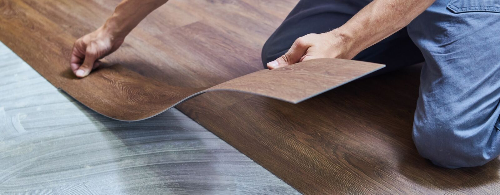 Handwerker verlegt braunen PVC-Boden auf einer mit Kleber vorbereiteten Betonunterlage.